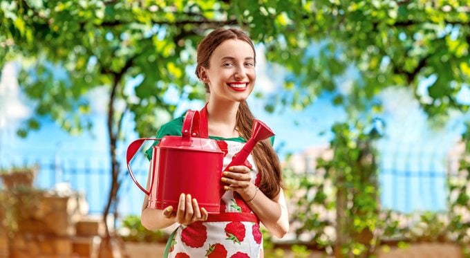 Portrait of a young woman gardener with apron and watering can in the garden