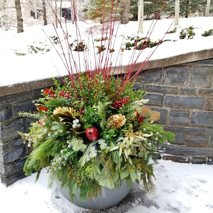 A gray winter planter with assorted greenery, a pomegranate, red twigs and berries.