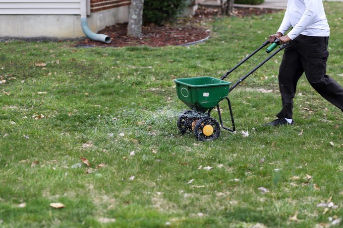A African American Man Using A Seed And Fertilizer Spreader On A Front Lawn